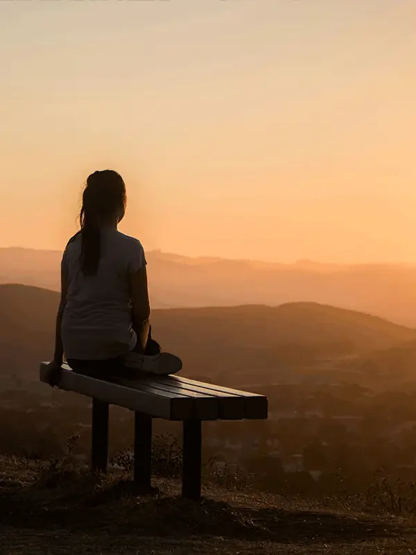 Eine Frau sitzt auf einer Bank und blickt in den Sonnenuntergang – ein Moment der Stille inmitten des Wandels. Dieses Bild erinnert daran, dass Veränderung nicht nur Dynamik bedeutet, sondern auch die Chance bietet, innezuhalten und neue Perspektiven zu gewinnen.